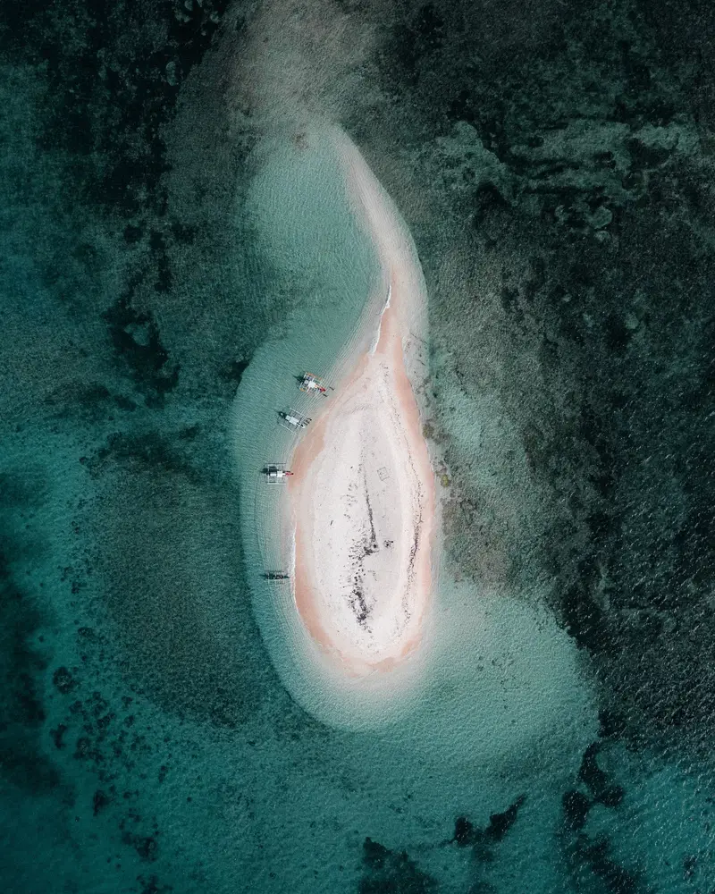 Aerial view of a teardrop-shaped white sandbar ringed by reef near Carnaza Island, Cebu