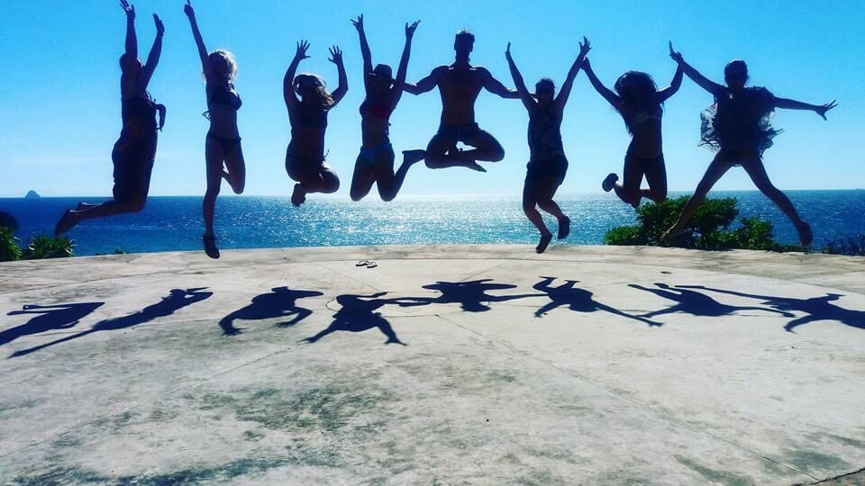 Group jumping in unison on rocks above a blue sea