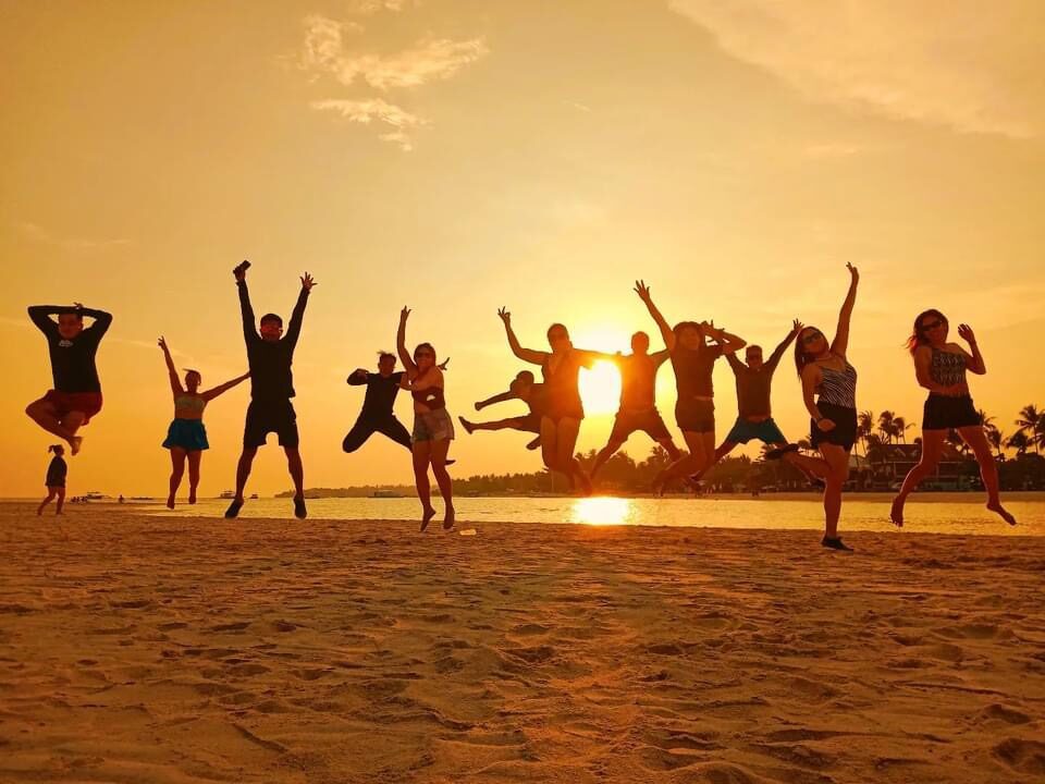 The whole group leaping on the sand in front of a golden sunset