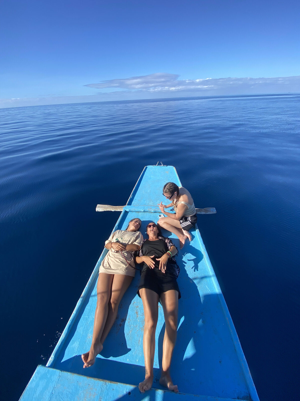 Guests lying back on the bow of a bangka boat on a mirror-flat sea