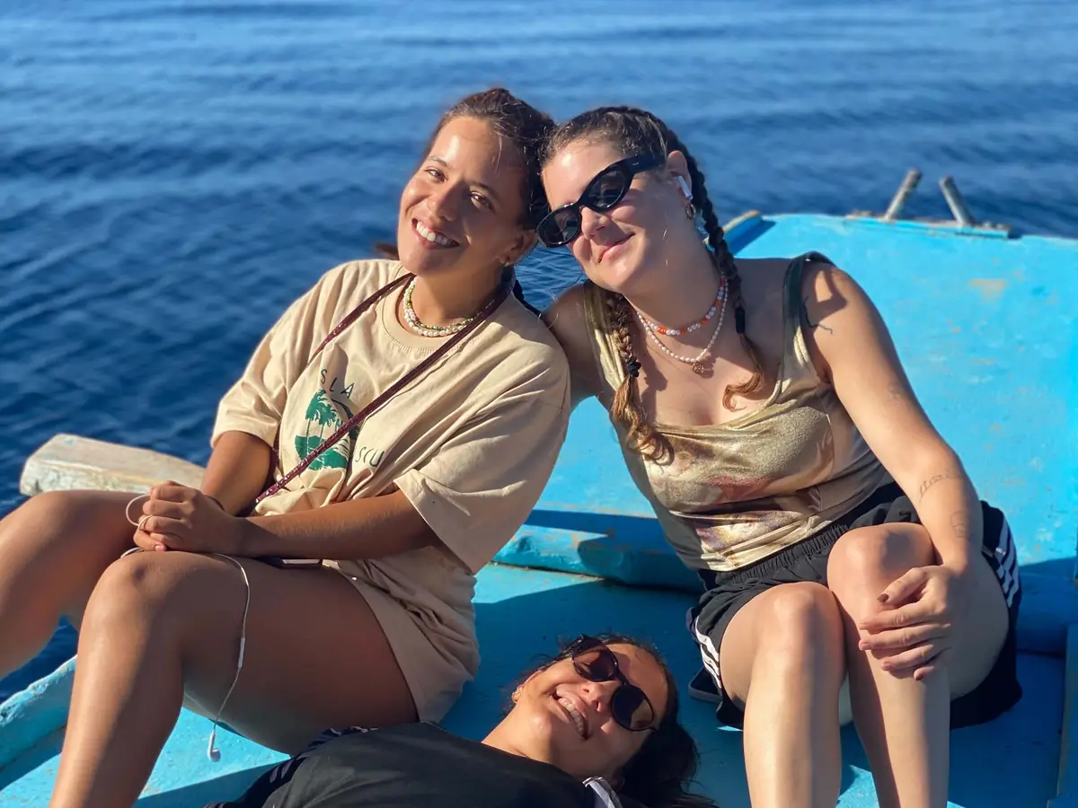 Three guests laughing together on the sunny bow of the bangka