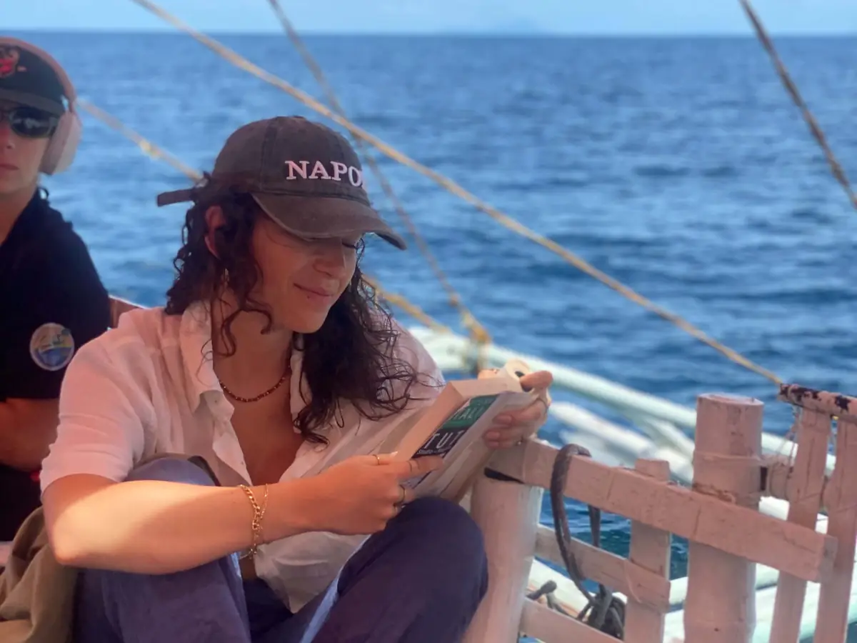 A guest reading a book in the shade of the bangka's canopy at sea
