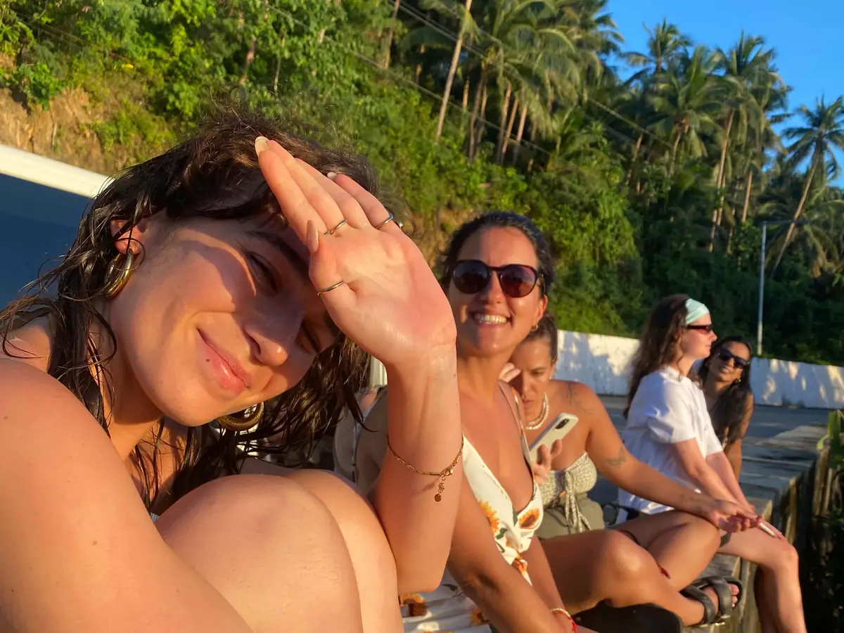 Guests smiling in the golden-hour sun on a roadside wall lined with coconut palms