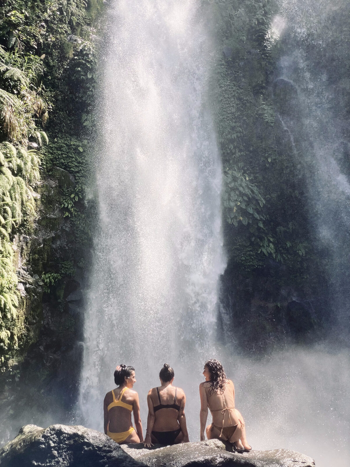 Three travellers resting at the foot of a jungle waterfall