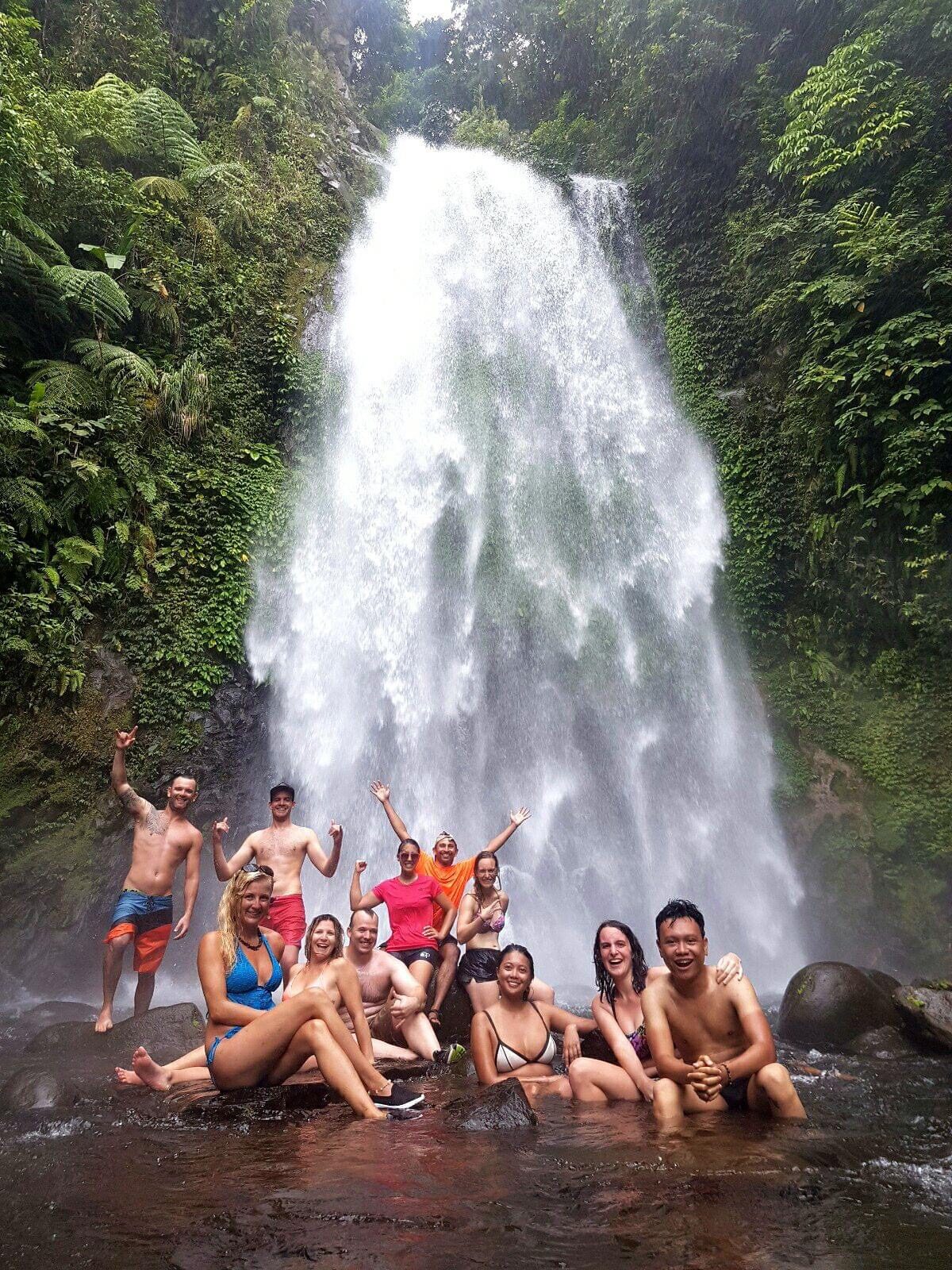 Large tour group gathered at the base of a tall waterfall