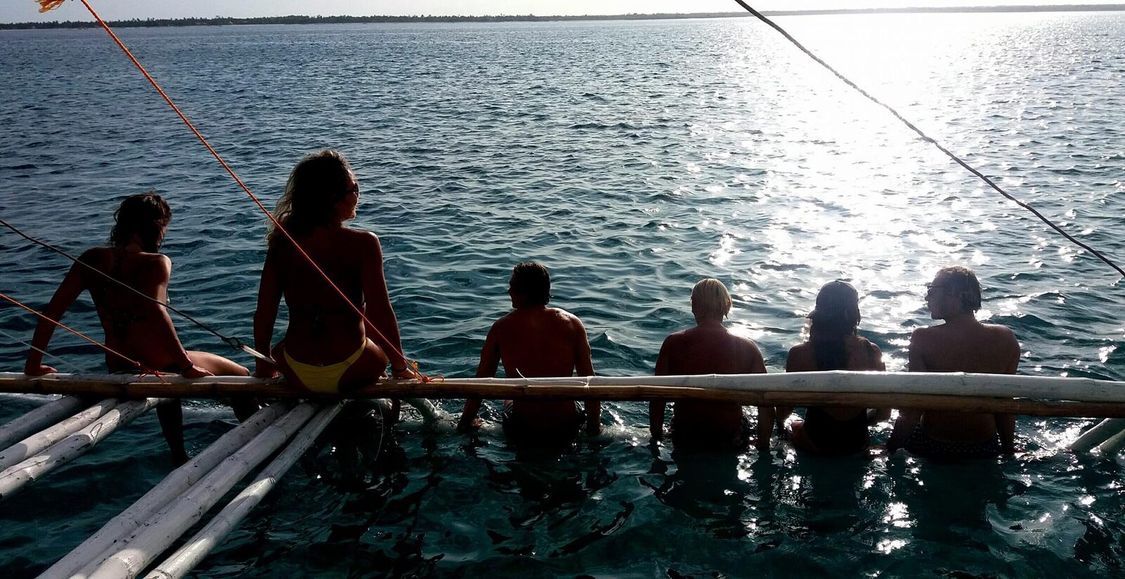 Group sitting along a bamboo outrigger over the water at dusk