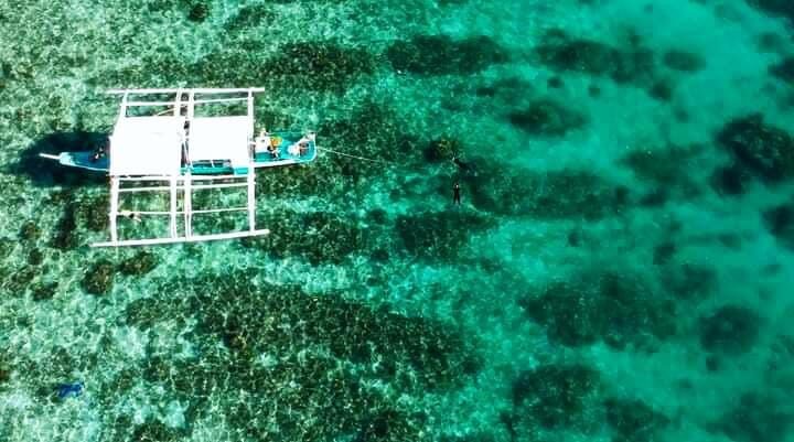 Aerial view of an outrigger boat above a turquoise coral reef
