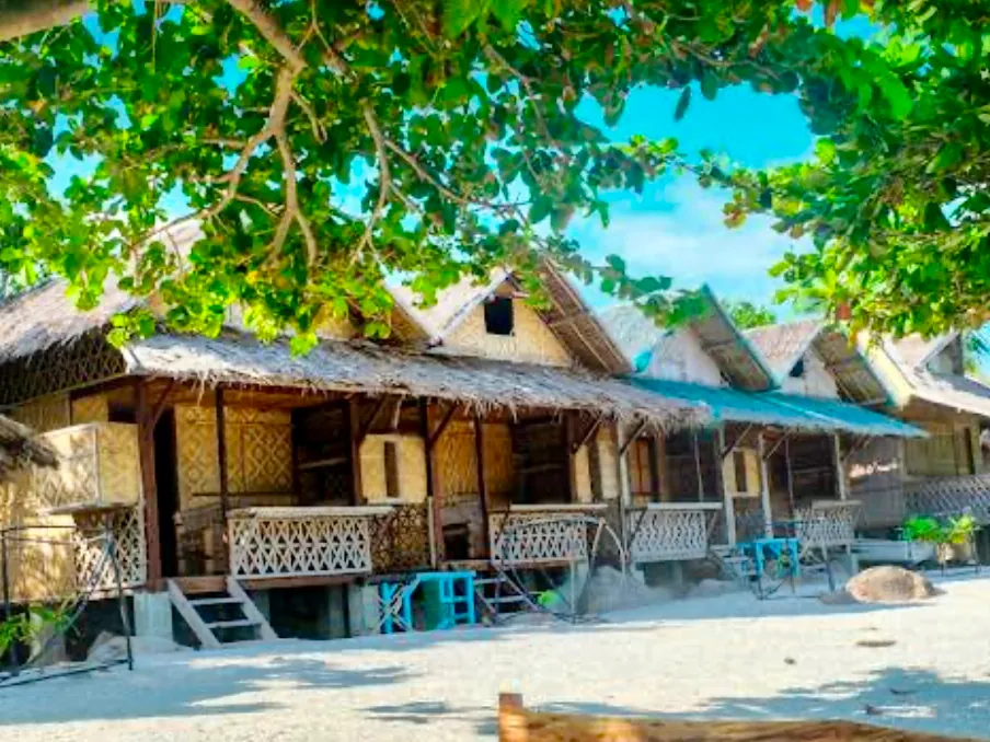 Bamboo beachfront bungalows shaded by trees on Sambawan Island