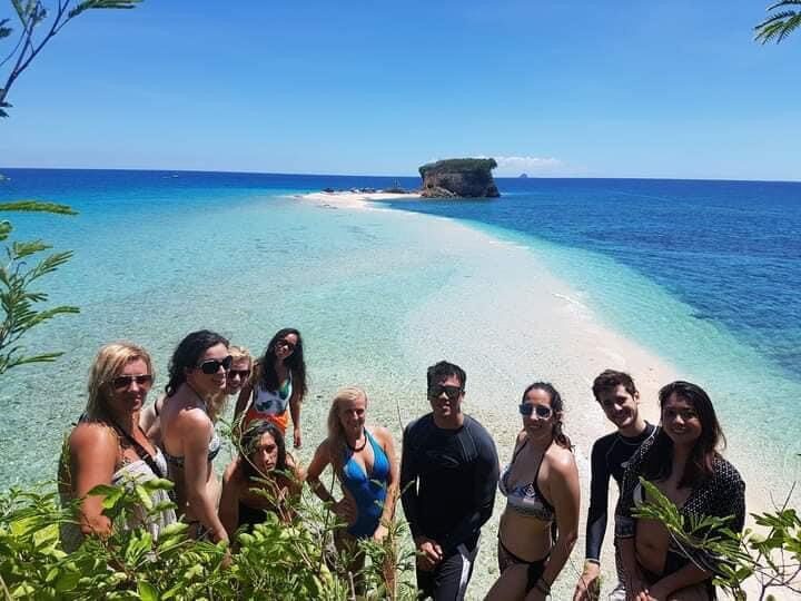 Tour group posing together on a white sandbar with a rock islet behind