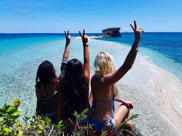 Three friends throwing peace signs on a turquoise-fringed sandbar