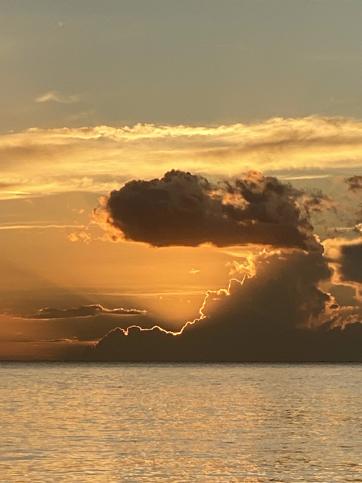 Dramatic cloud lit gold by the setting sun over a calm sea