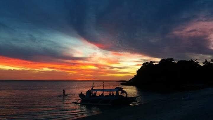 A boat silhouetted against an orange sunset on the water