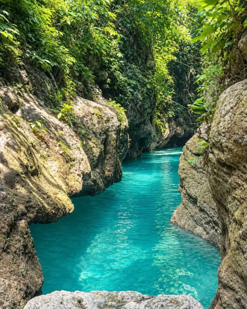 A narrow turquoise channel between mossy limestone walls in the Badian canyon
