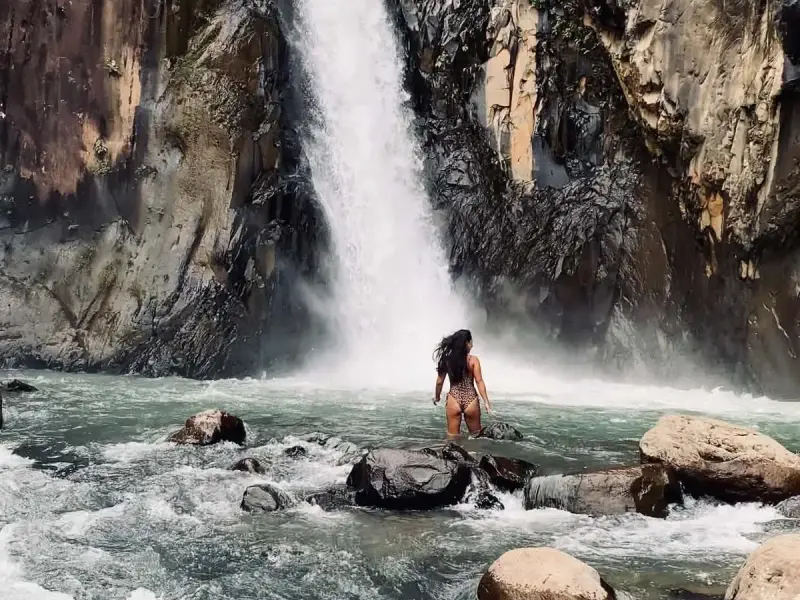 A guest wading toward a waterfall that pours down a dark rock canyon in Biliran