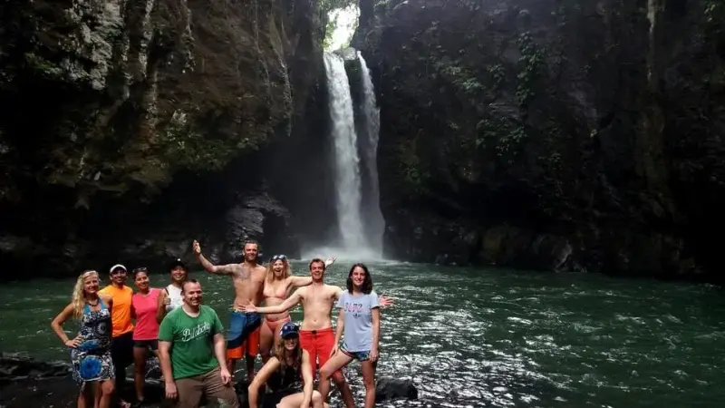 A group of guests standing in the pool below a tall waterfall in Biliran