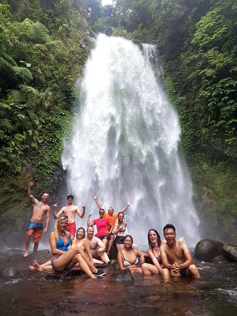 Large tour group gathered at the base of a tall waterfall
