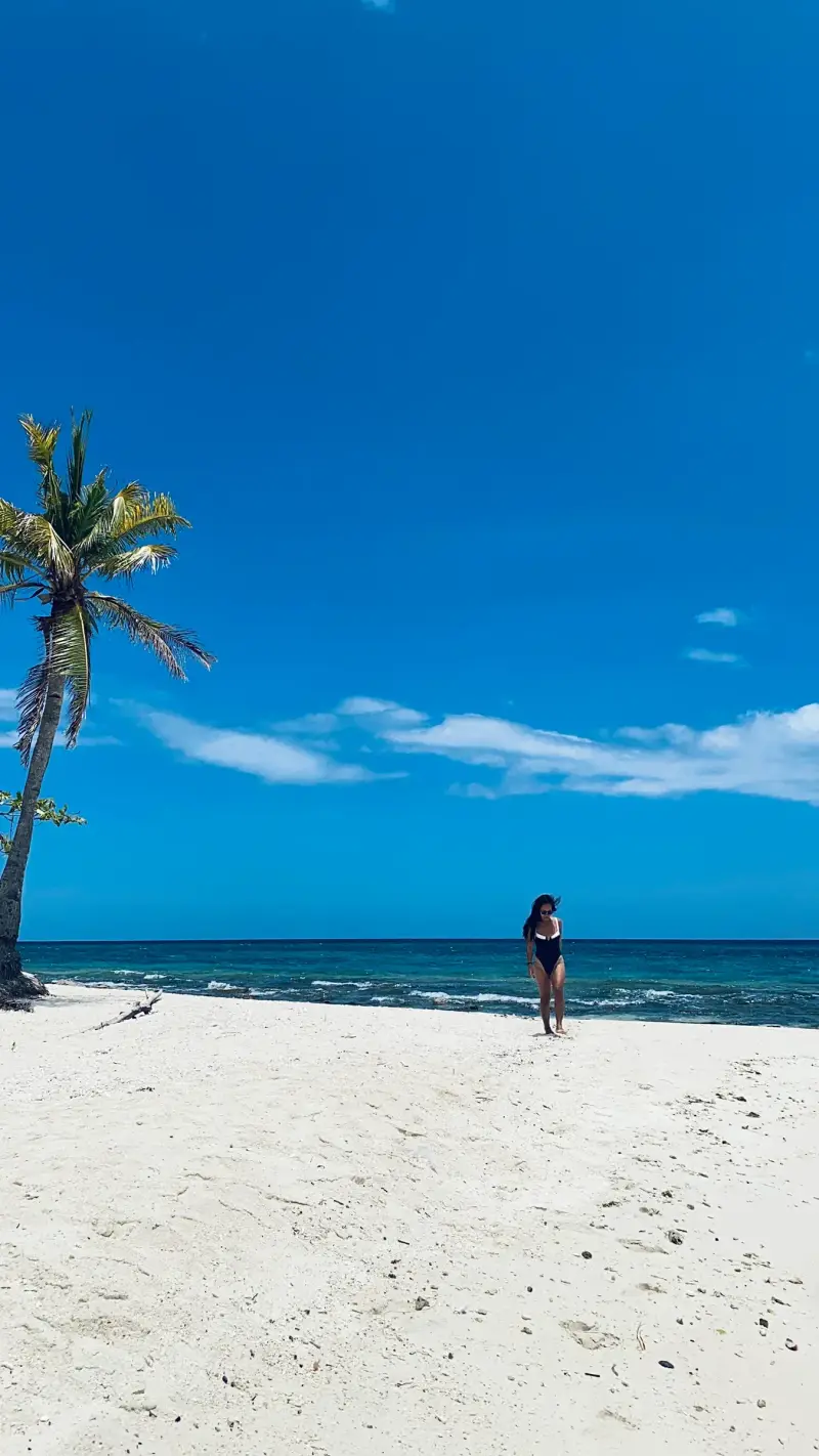 A guest on Kalanggaman's wide white beach beside a leaning palm