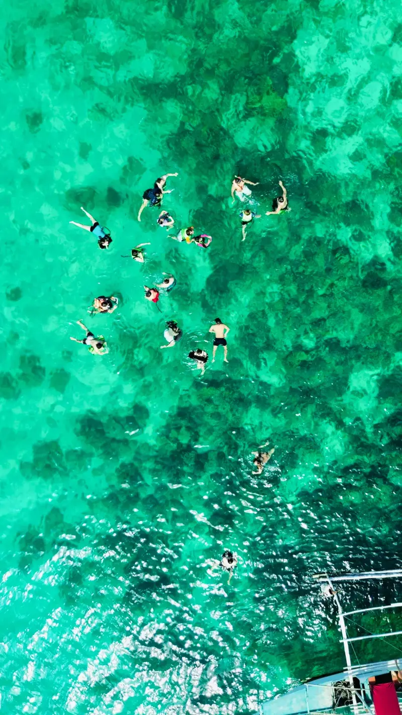 Drone view of a group of snorkellers floating over a green-blue reef off Malapascua