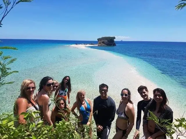 Tour group posing together on a white sandbar with a rock islet behind