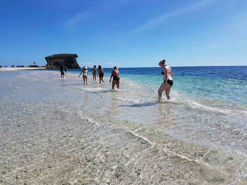 Travellers wading through clear shallow water near a rock islet