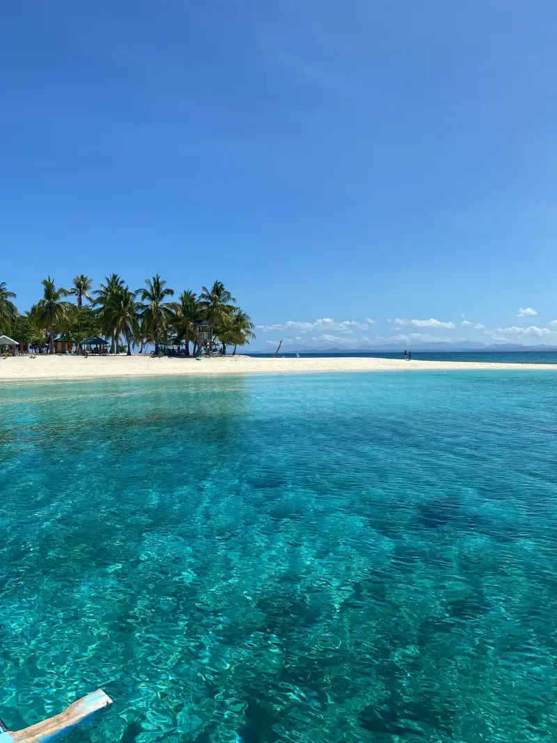 Clear turquoise shallows leading to a white beach and coconut palms at Virgin Island